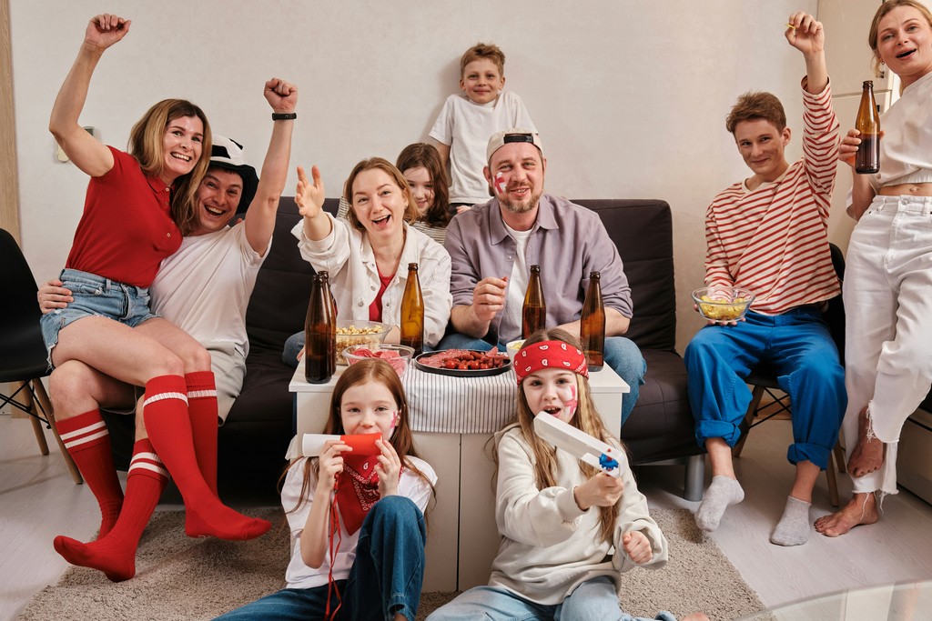 A lively group of friends and family celebrating together in a living room, with some cheering and others enjoying snacks and drinks, creating a festive atmosphere.