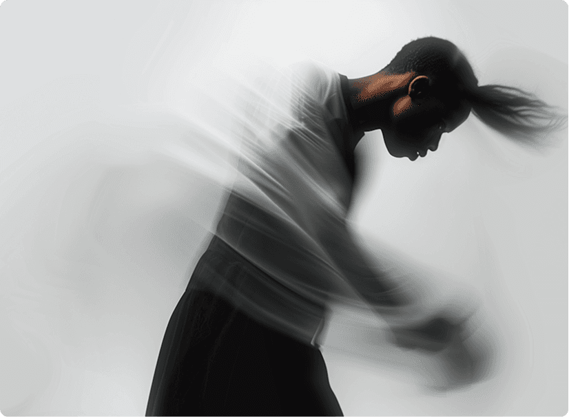 A person gracefully moves in a dynamic dance, captured mid-motion with blurred arms and a ponytail, against a minimalist white background.
