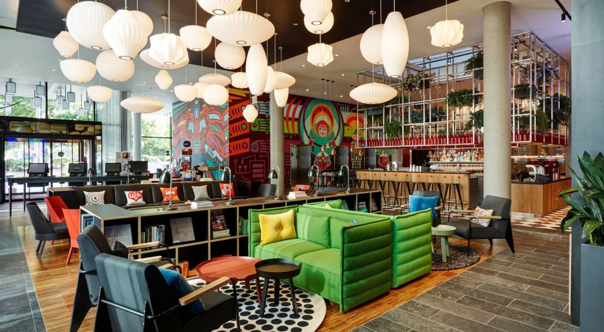 A vibrant hotel lobby showcasing lime green sofas, contemporary bubble lighting, floor-to-ceiling murals, and a lushly planted bar as a striking backdrop.