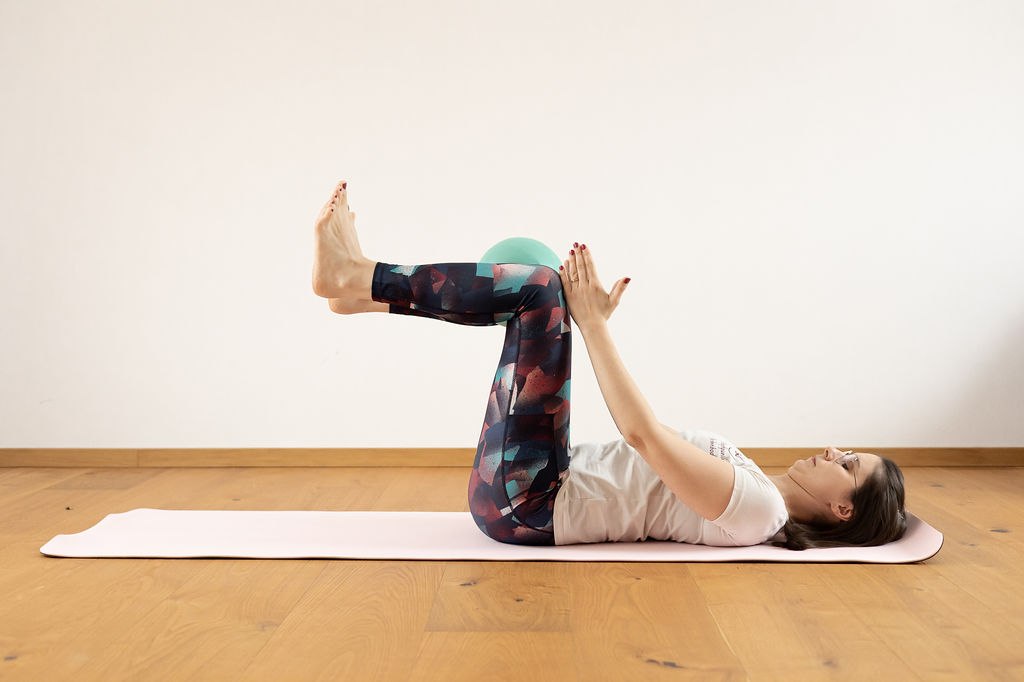 Smiling female therapist with short gray hair, wearing a brown top and a purple shawl, surrounded by a cozy background.