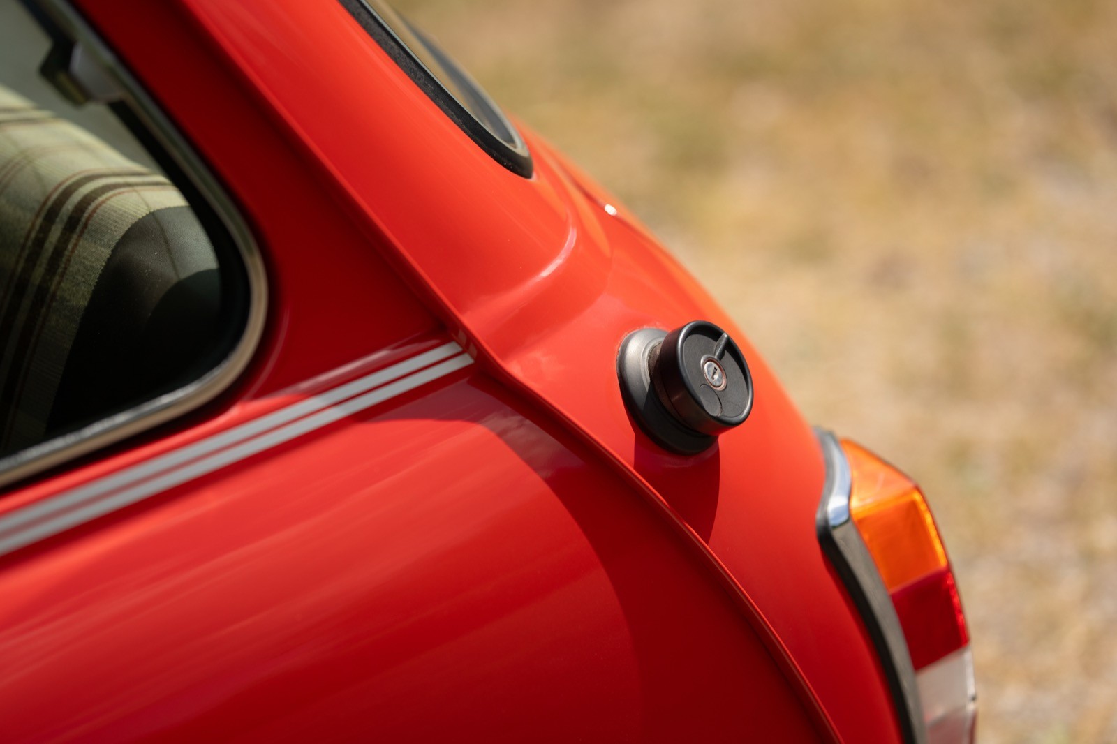 Close-up of a red car's rear corner, showing a fuel cap and part of the bodywork.