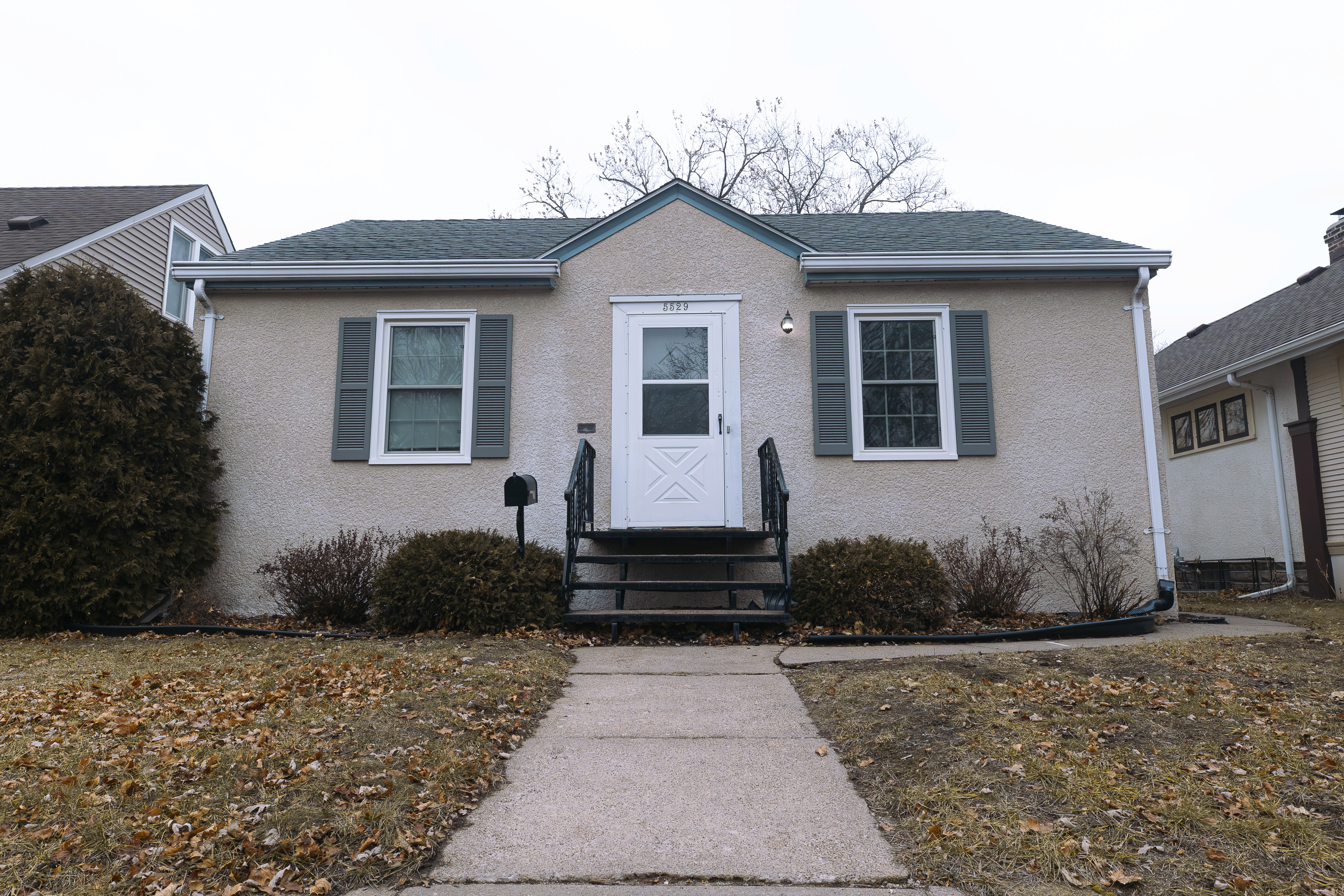 Exterior view of a single-story residential home with a sidewalk under an overcast sky.