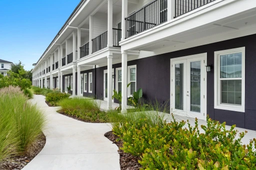 A clear view of the walkway leading to the entrance of the apartment building, lined with greenery and well-maintained pathways.