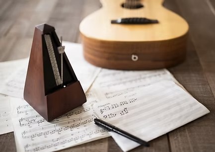 Ein Metronom steht auf Notenblättern neben einer Gitarre – Förderung junger musikalischer Talente durch die DAG.