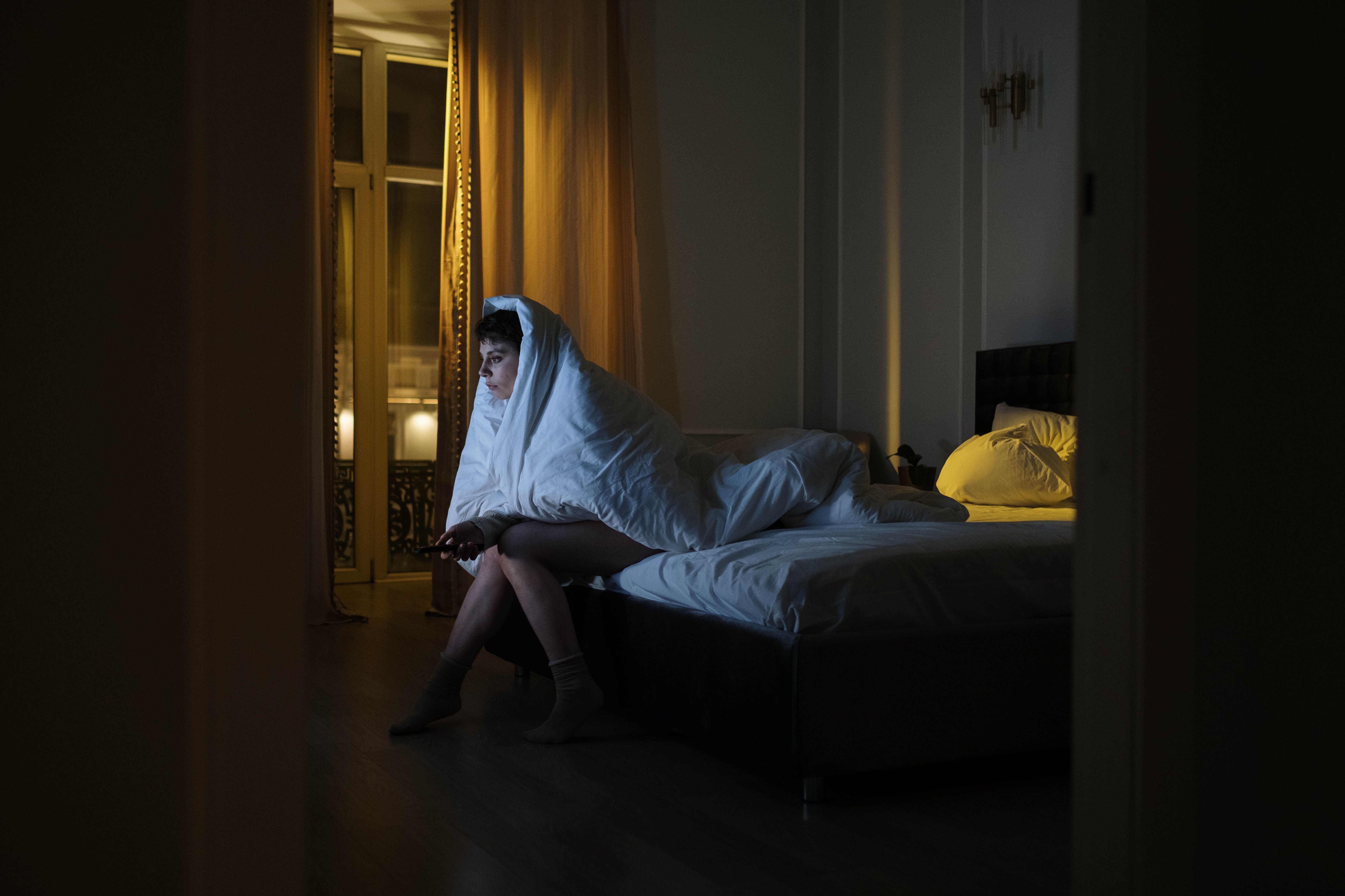 Woman sitting up in bed wrapped in a white blanket