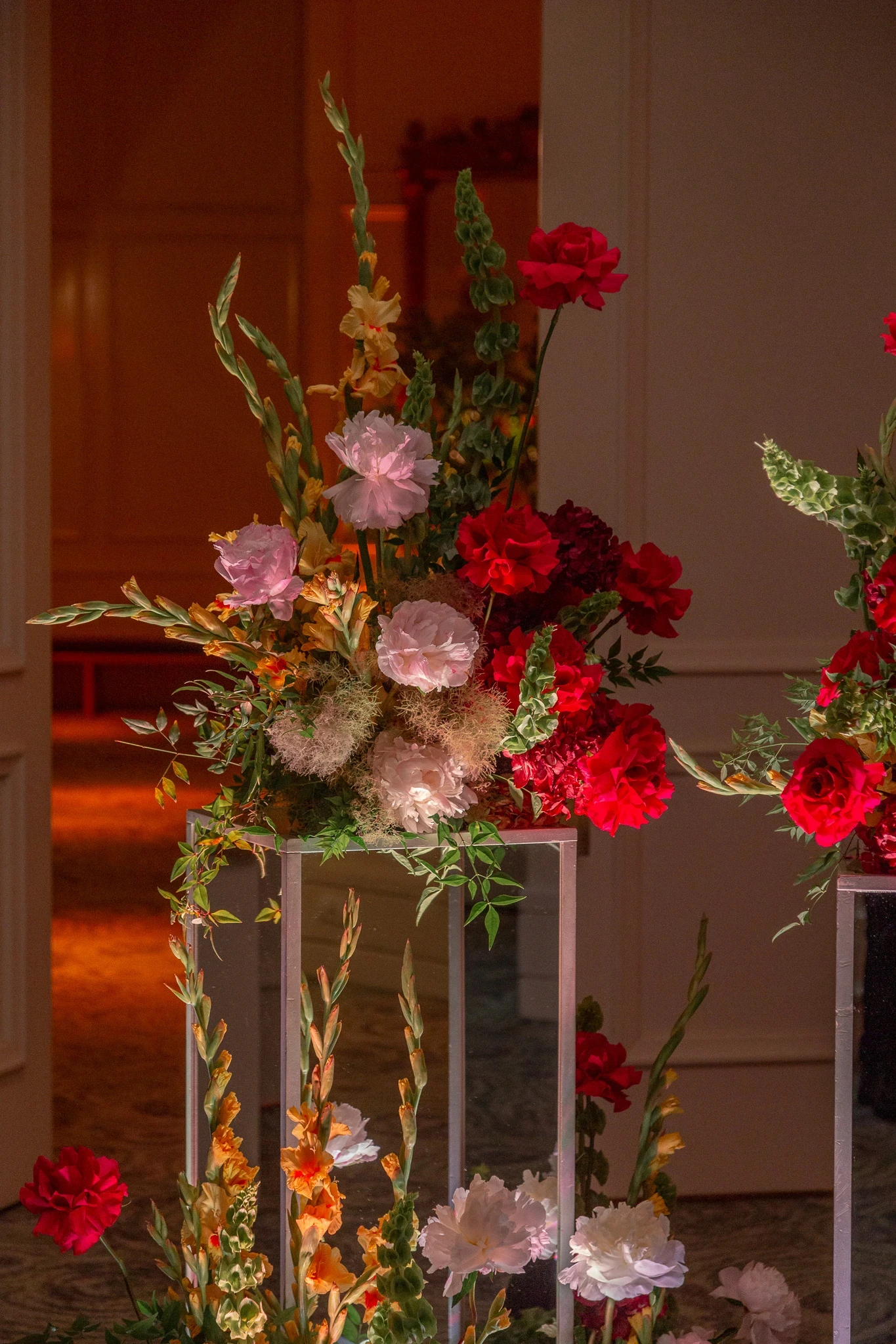 Estructura minimalista transparente con flores de tallo alto como gladiolos y rosas en tonos vibrantes.