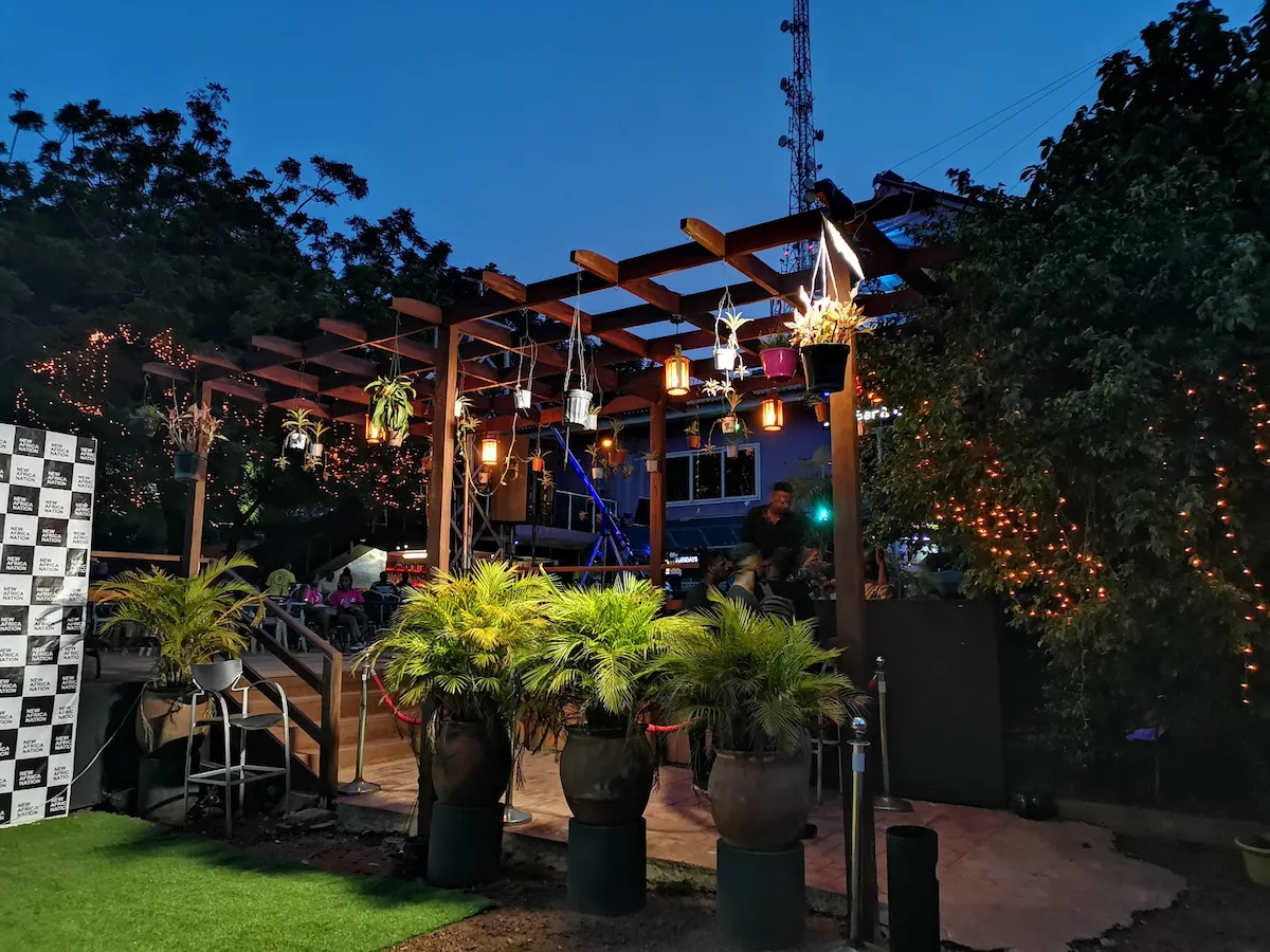 Outdoor terrace with a wooden pergola, hanging plants, and warm fairy lights in Accra, Ghana.