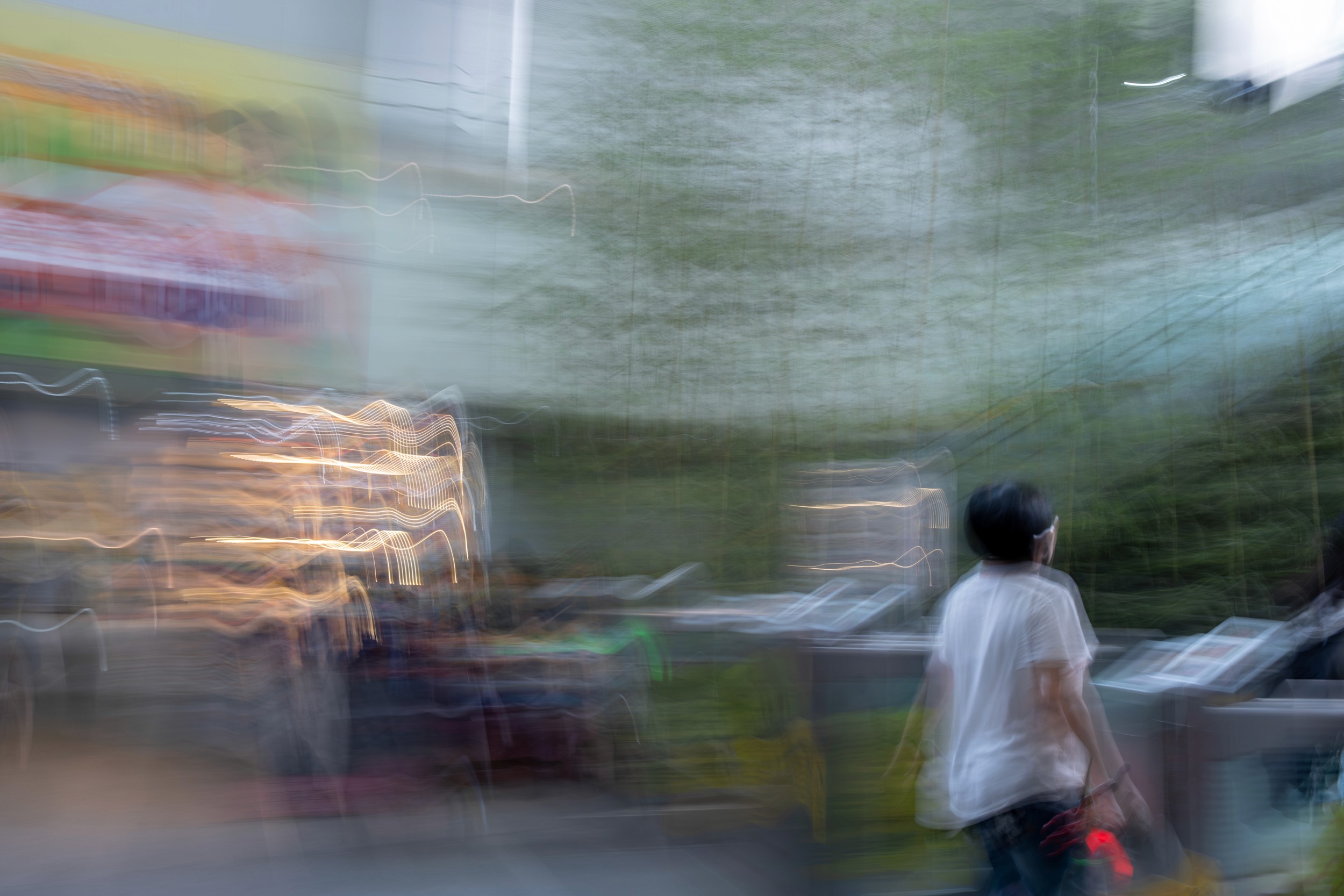 Color motion blur photograph of a person walking past bright storefront lights with streaks of neon swirling through the frame.