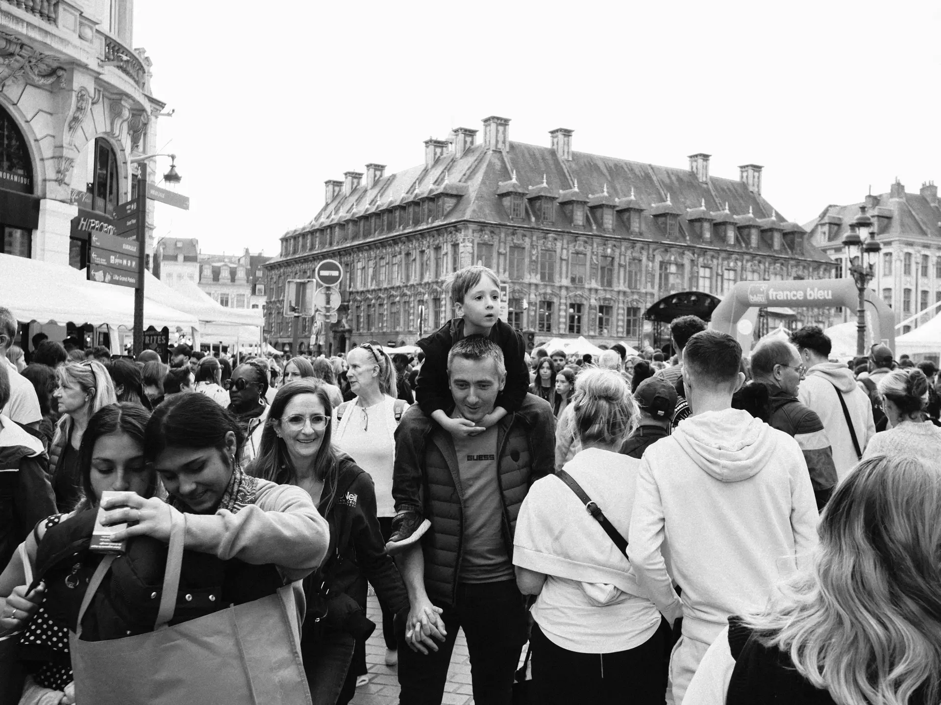 Crowded square with a child on someone’s shoulders, in black and white