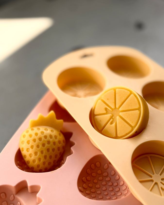 Mango coconut gummies in citrus and strawberry shapes, set in silicone moulds on a light surface.