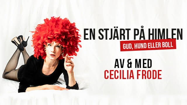 A young person with curly hair smiles at the camera while sitting in front of a laptop against a dark background.