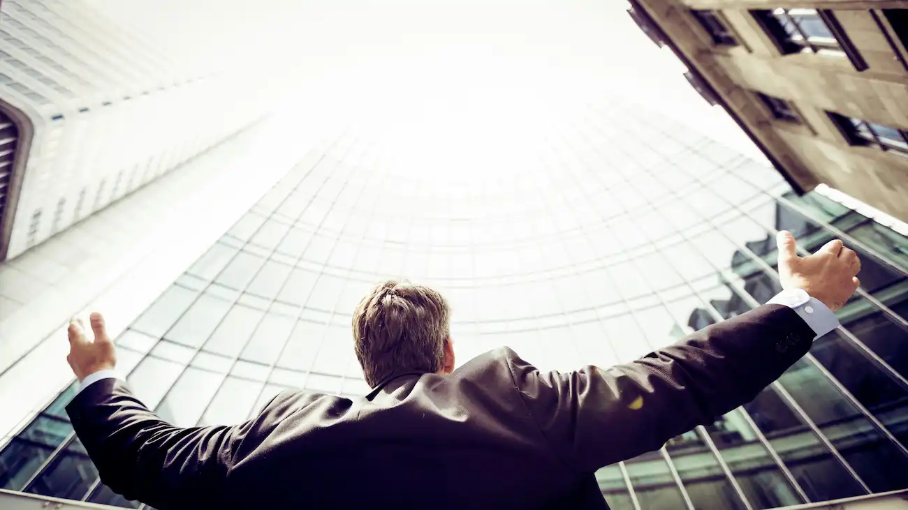 Businessman in a suit with arms raised between tall office buildings — illustrating the benefits of sports sponsorship for clubs, including growth, credibility, reach and stronger sponsor networks.