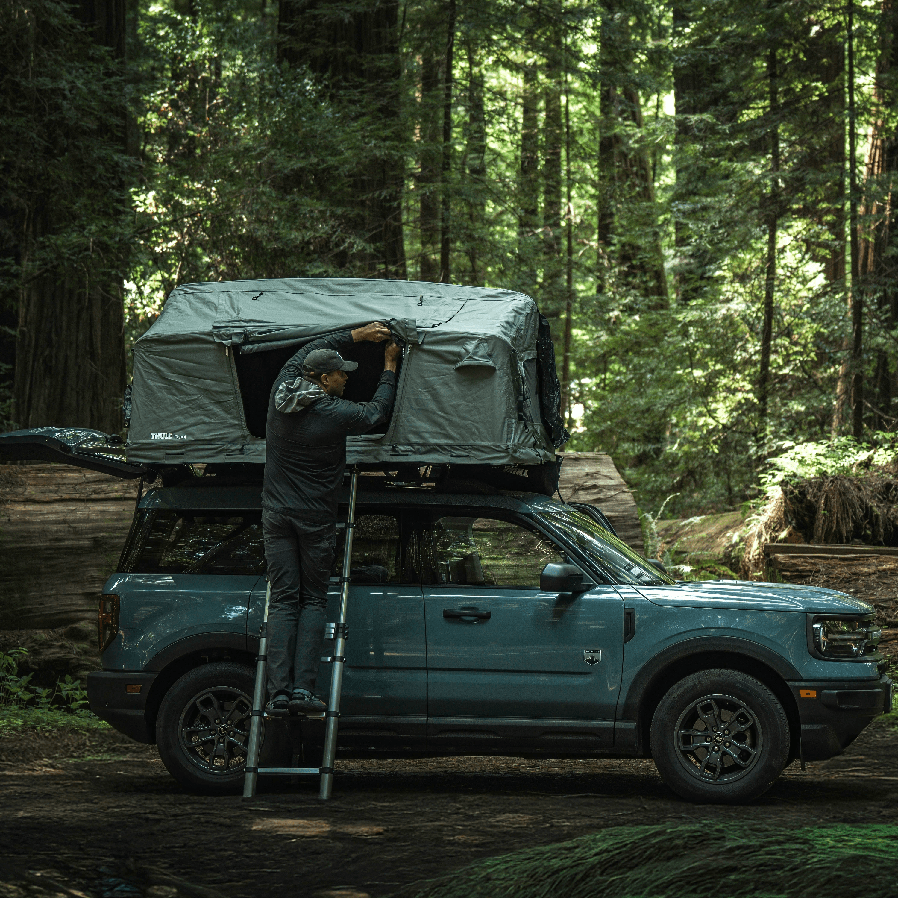 Person setting up rooftop tent on suv in forest.