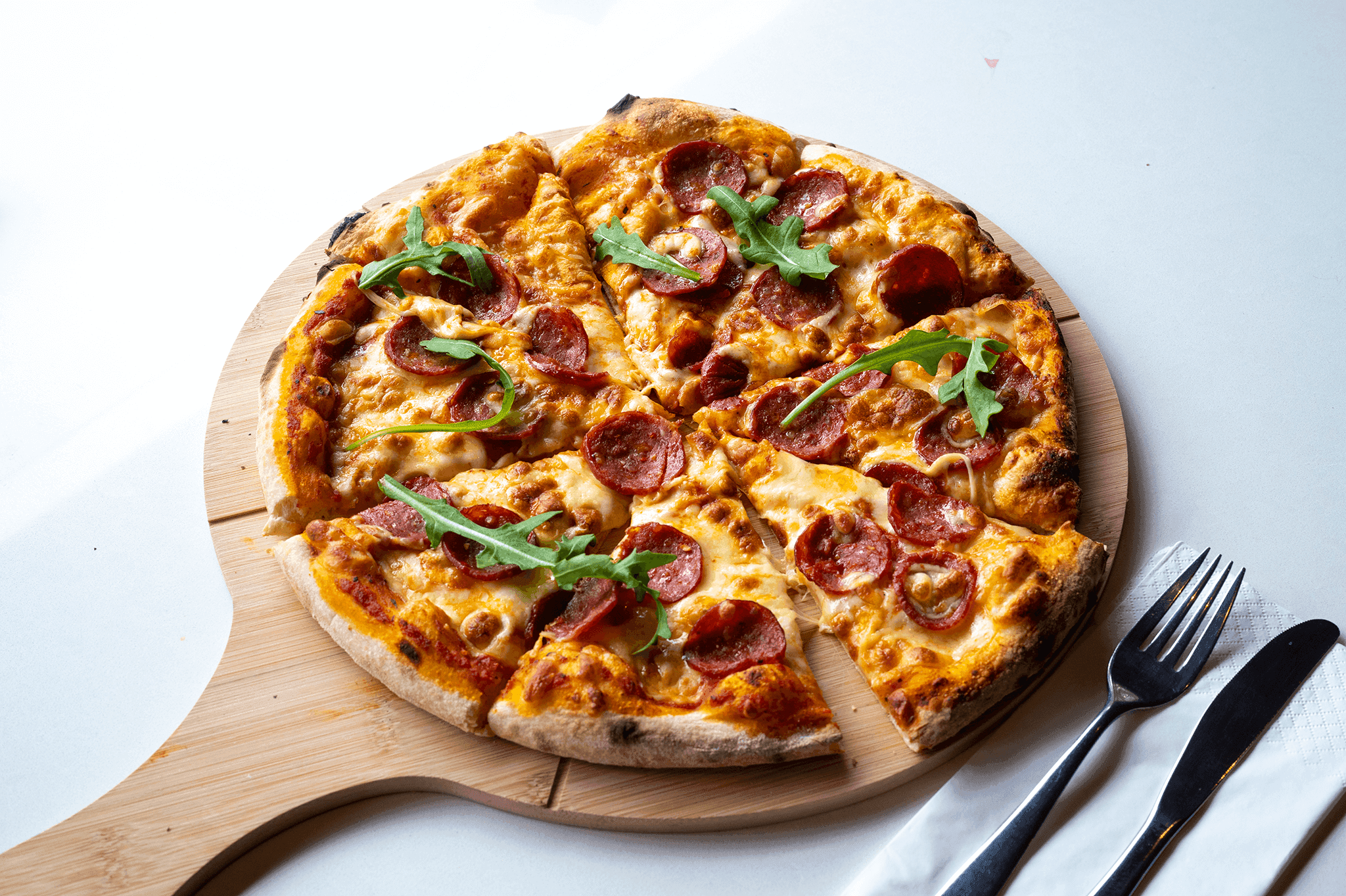 Freshly baked pepperoni pizza being taken out of the wood-fired oven, topped with arugula.