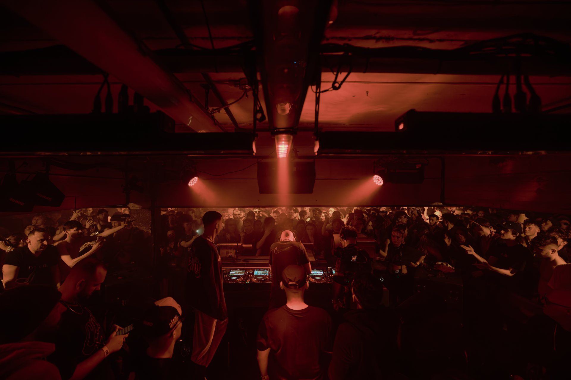 Crowd around the DJ booth under red light at IDRA
