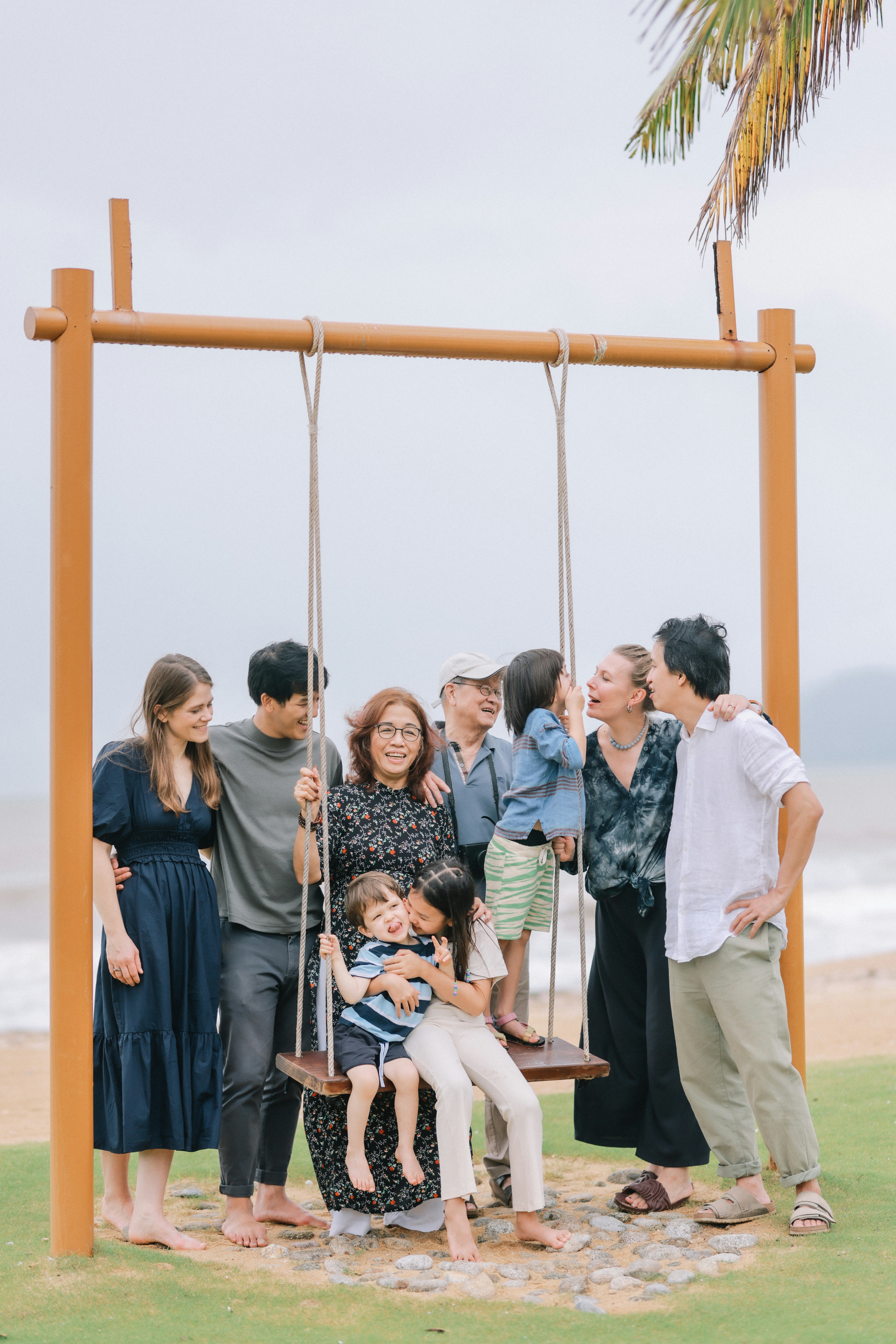 A multi-generational family posing on a swing by-the-sea swing.