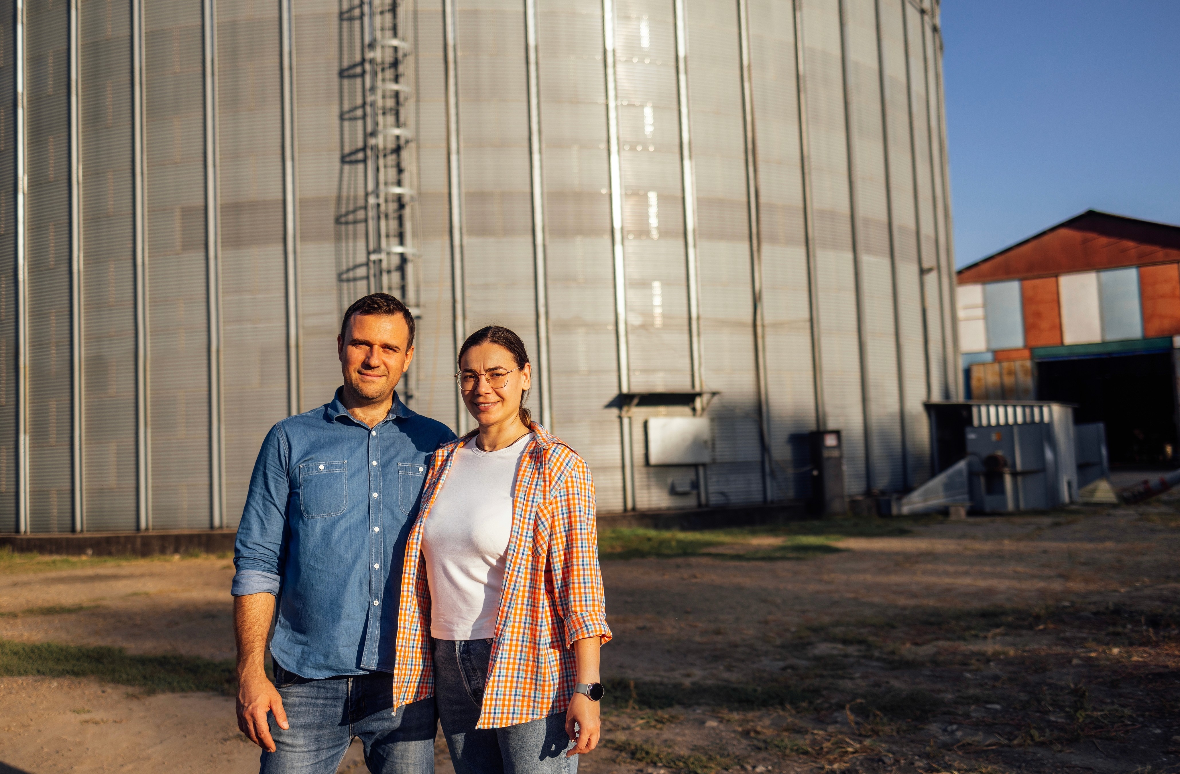 Two agricultural professionals standing in front of a grain silo at sunset