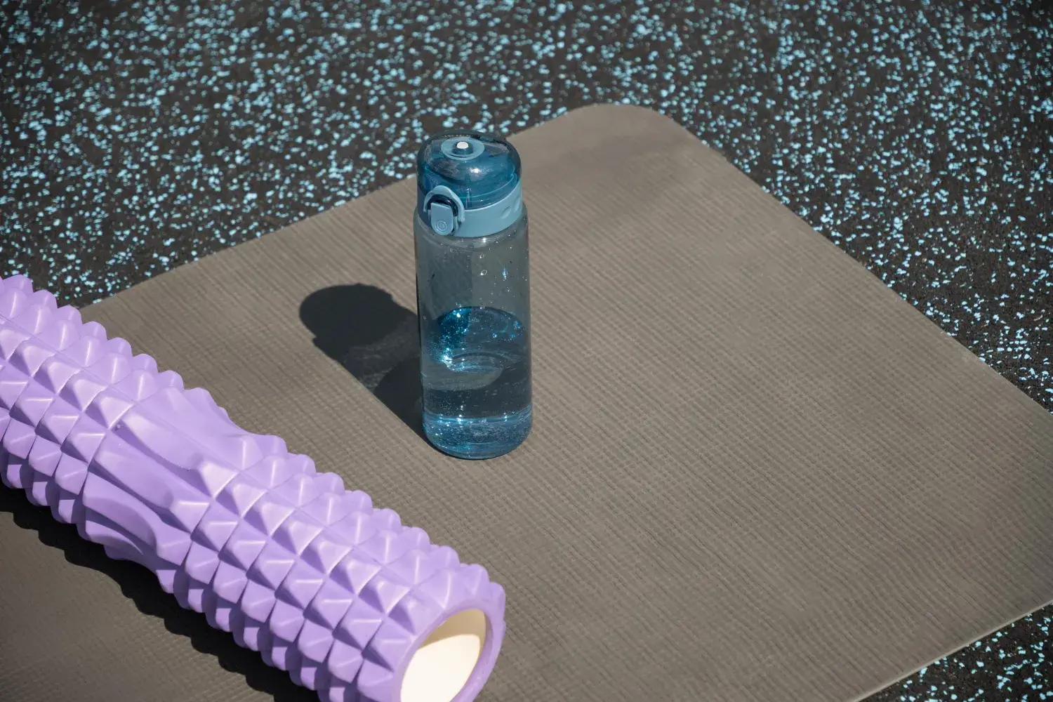 A foam roller on a yoga mat with a water bottle