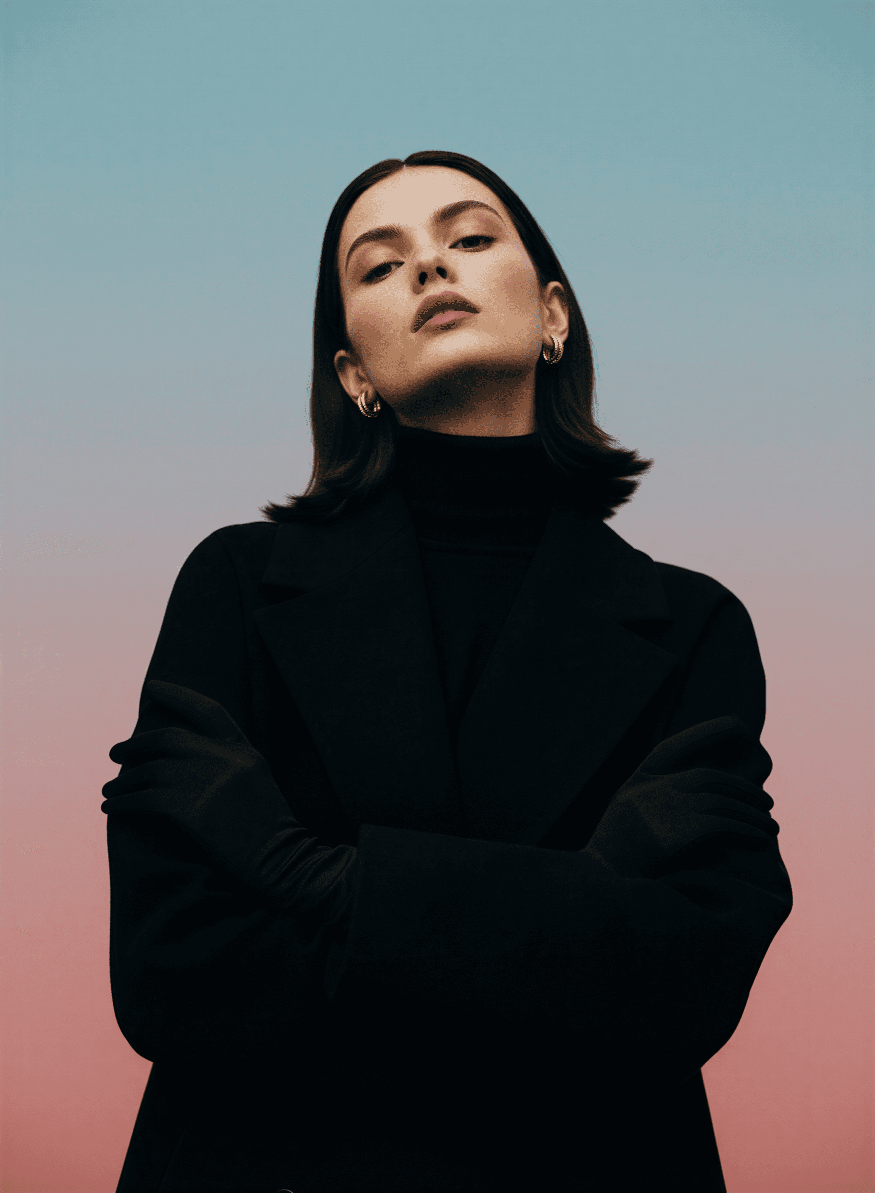 A woman in a black coat, arms crossed, calm gaze