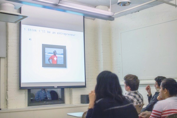 A photo of a group of people sitting in a classroom and watching a picture on a screen projector.