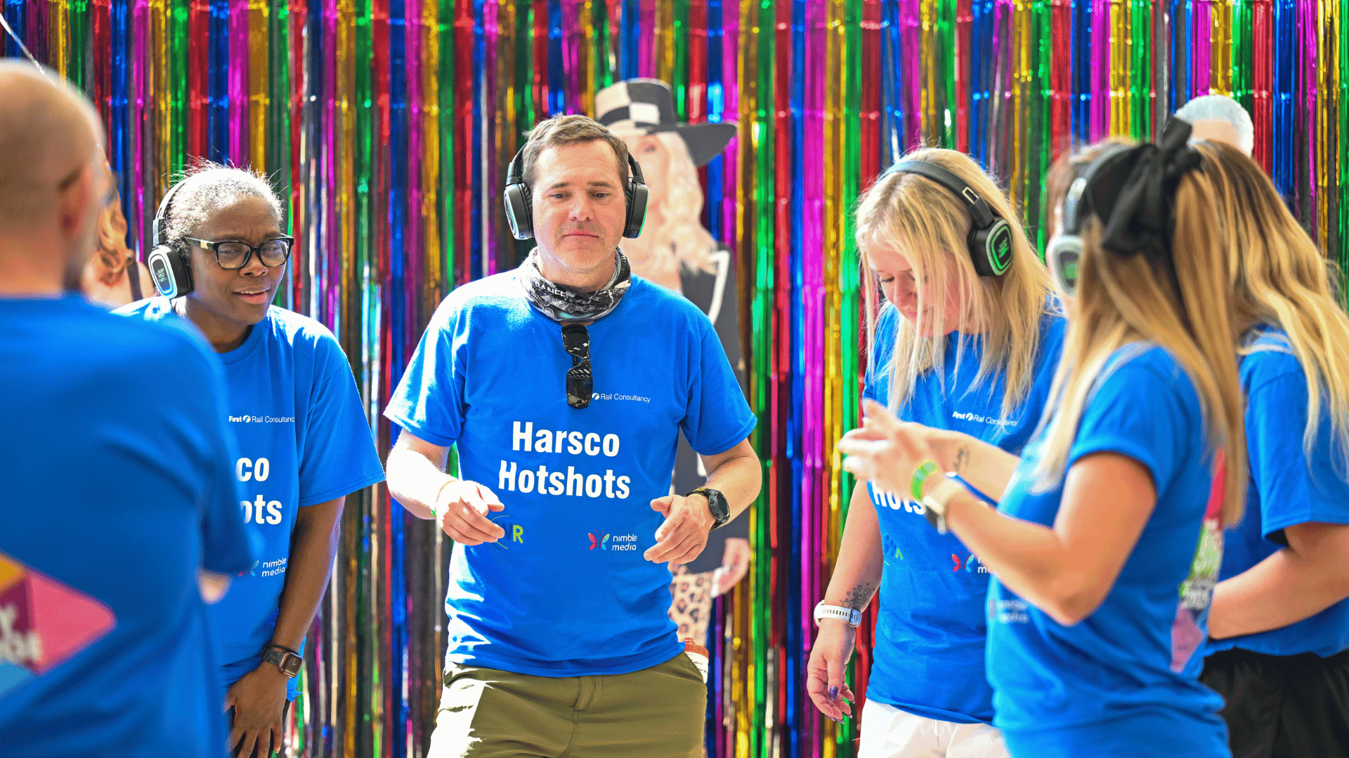 Outdoor team-building event with participants wearing matching blue shirts, taking part in inflatable obstacle courses and games, smiling and cheering, with the words 'ENTER A TEAM' in large bold white and green text across the image.