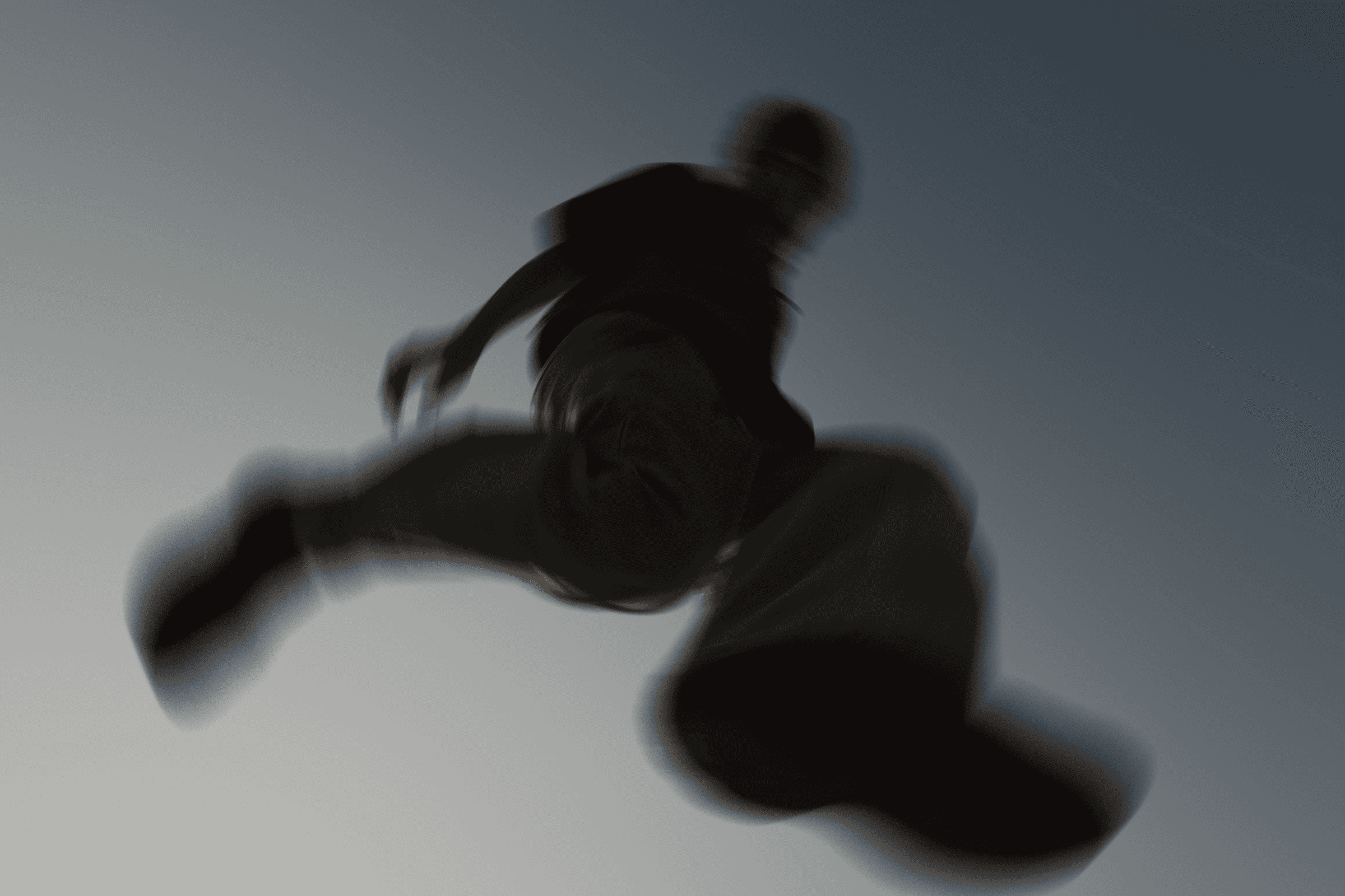 A low-angle, motion-blurred shot of a person jumping or running through the air against a clear, pale sky.