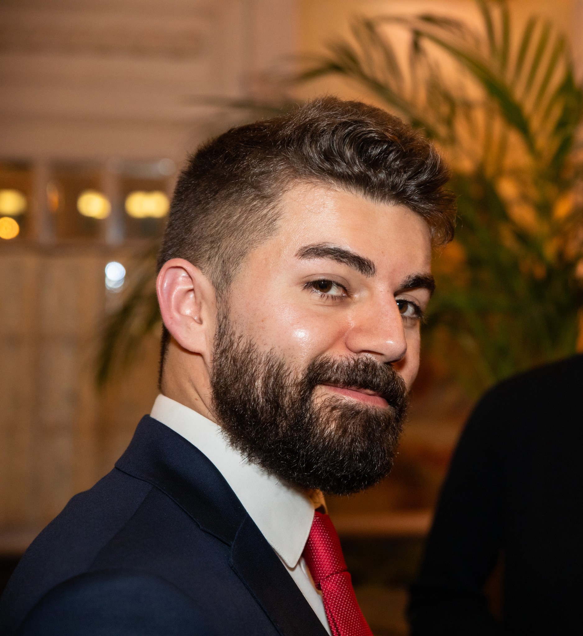 Un portrait en couleurs du designer Guillaume Normand regardant avec un sourire la caméra depuis son profil droit.