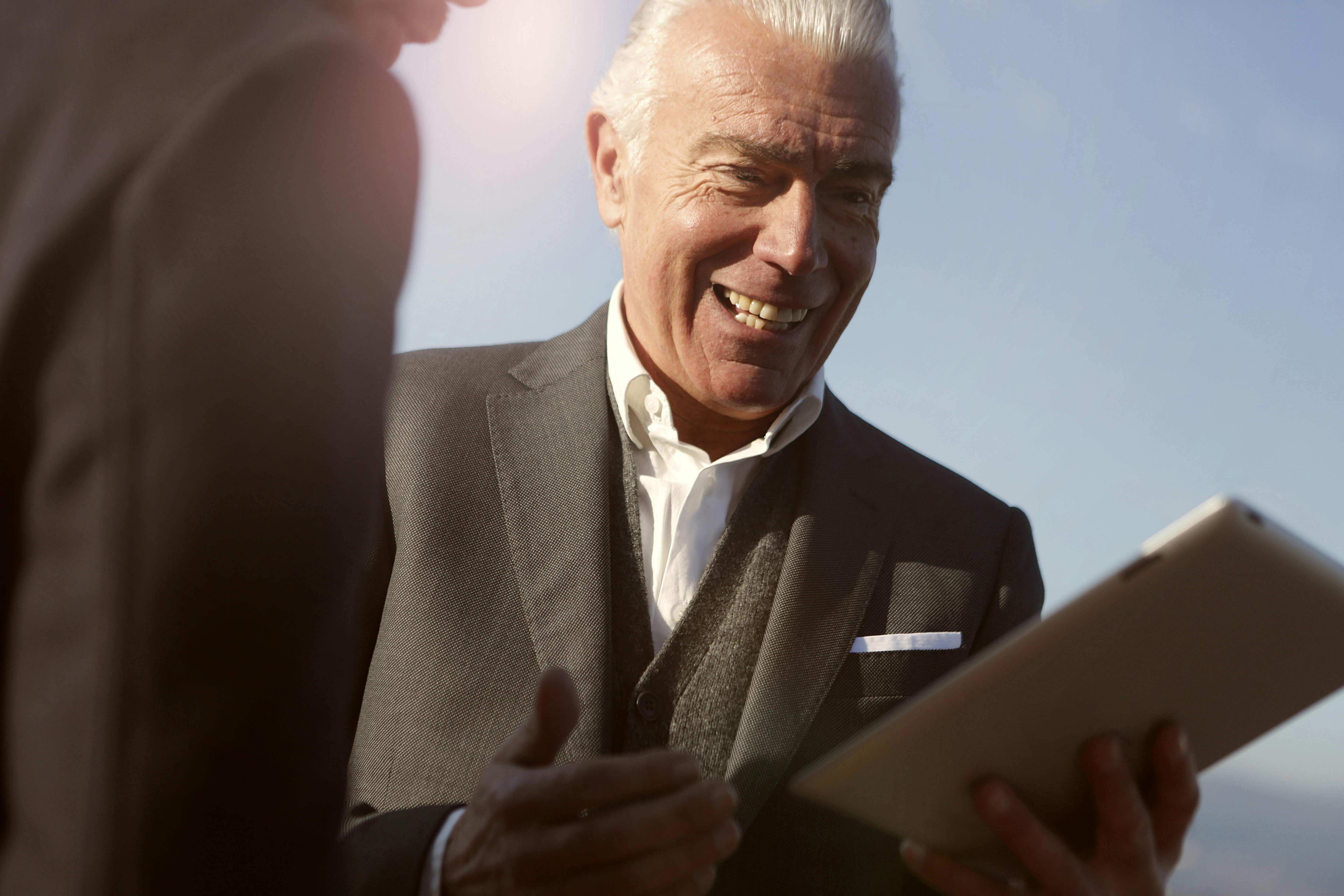 senior-businessman-smiling-while-interacting-on-a-tablet-with-a-colleague-outdoo - andrea-piacquadio (pexels)