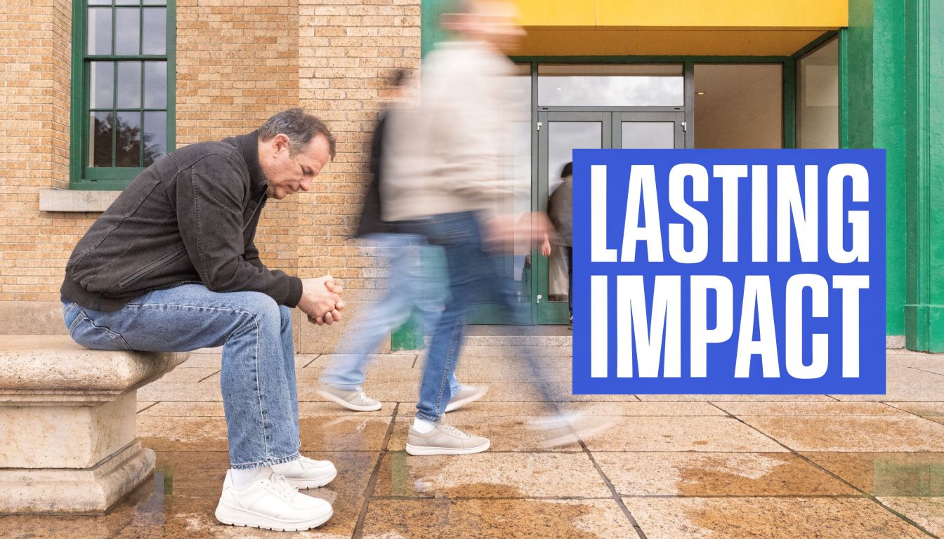 A man sits alone on a bench while blurred figures walk past him in front of a building.