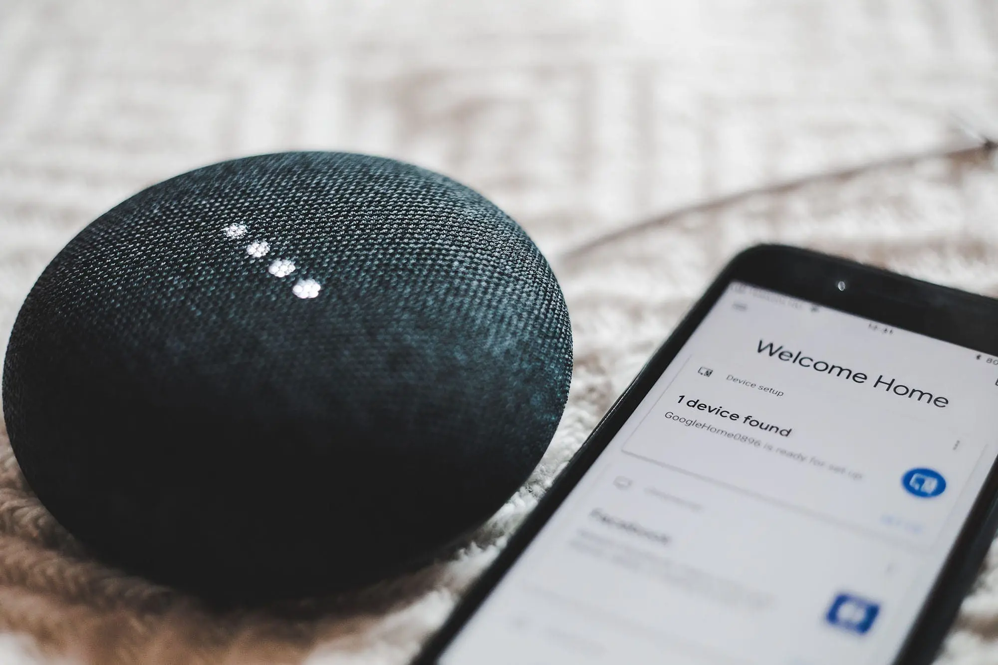 Smart speaker beside a phone showing a home device setup screen