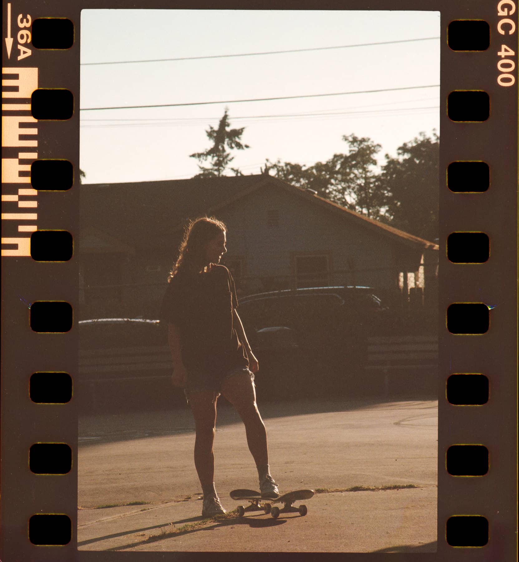A silhouetted figure stands on a skateboard at sunset, in front of a house. The warm, nostalgic tone is framed like a film strip, enhancing a vintage feel.