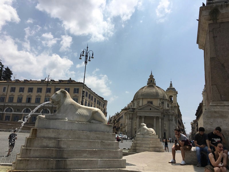 A photo of two stone lions sitting on a stepped pyramidal shape stone. Also from each lion's mouth there is a water flowing just like a fountain.