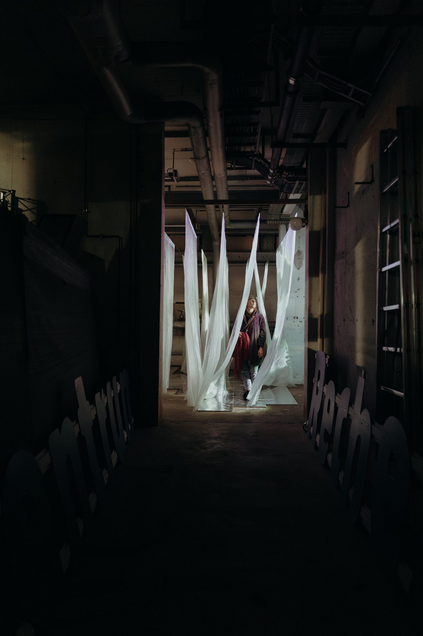 A person walking through a corridor of hanging translucent strips lit pink