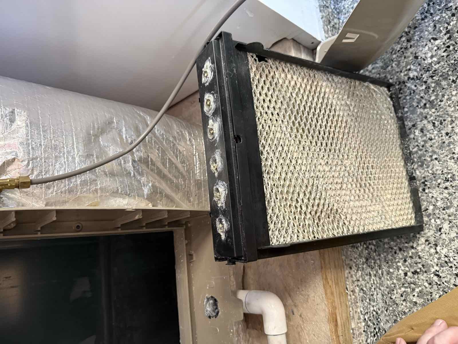 Furnace humidifier media pad removed for inspection, with mineral buildup on the water distribution ports.