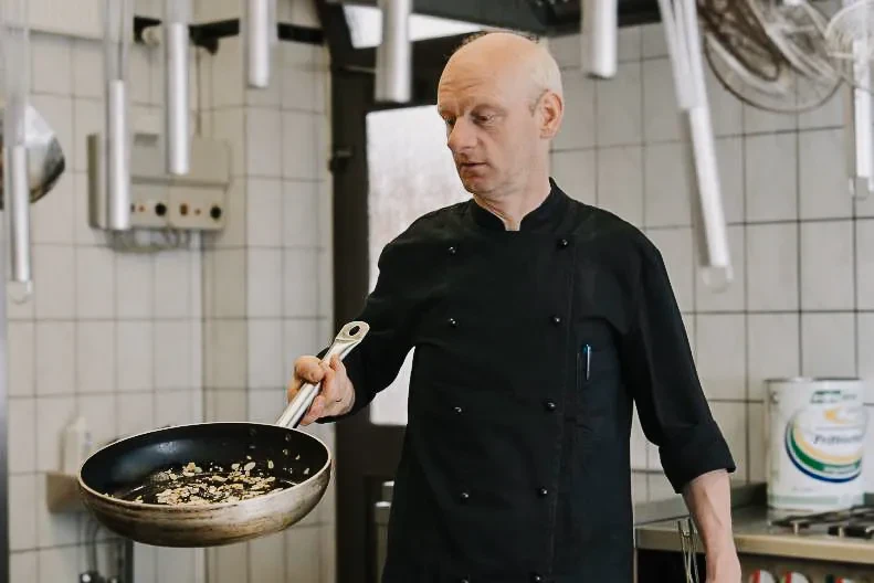 Heinz Wulfekotte mit einer Pfanne in der Hand am Kochen.