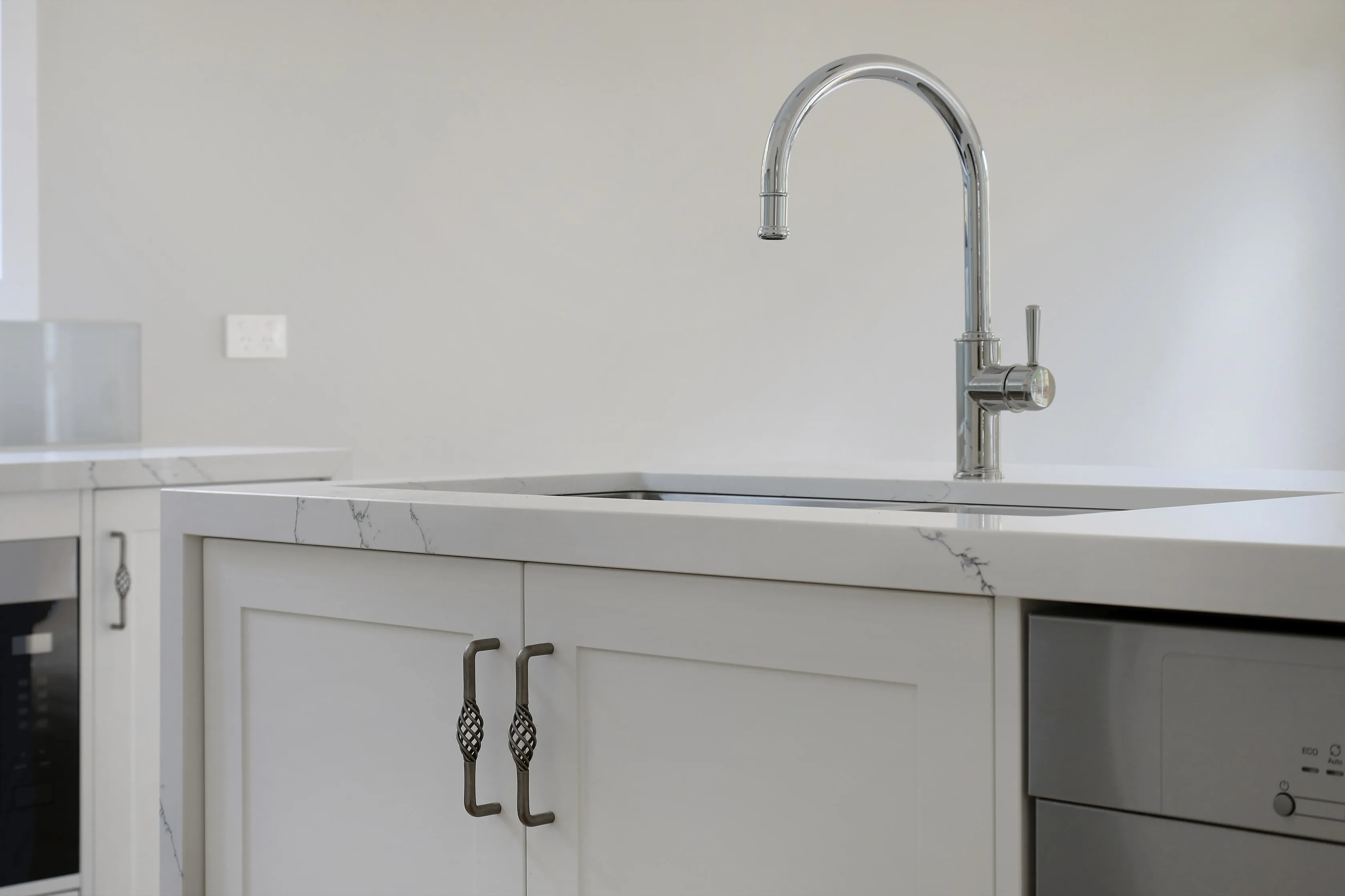 Kitchen island detail with a Calacatta-veined waterfall stone benchtop, undermount sink, chrome gooseneck tap, shaker cabinetry with iron handles and an integrated dishwasher