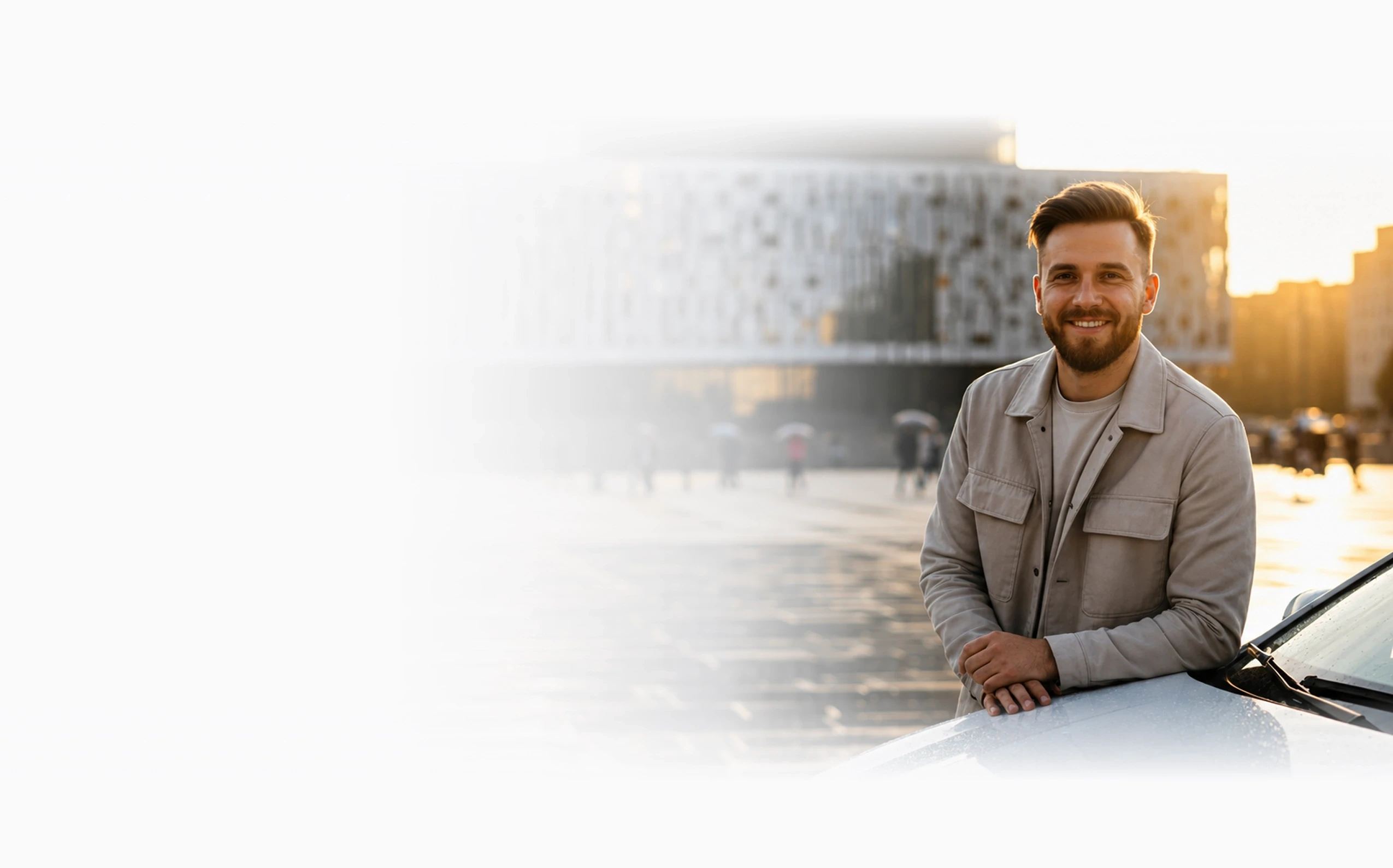 Man standing beside a car in a city square at sunset.