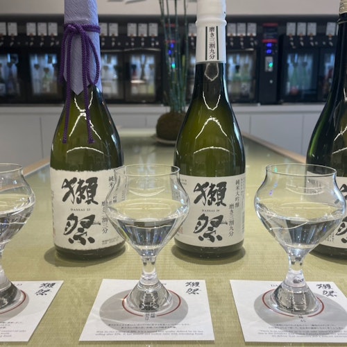 三杯清澈液體放在三瓶清酒前面，放在桌子上的杯墊上，背景現代化。