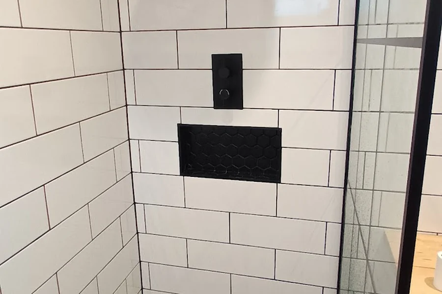 A finished shower: white metro tiles meeting at a mitred corner, with a black hexagonal tiled niche and a matt black control.