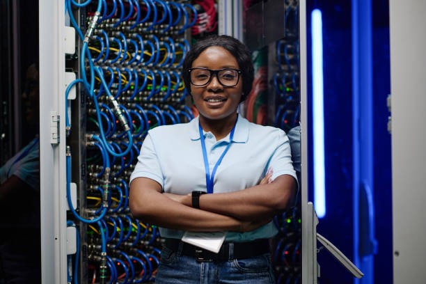 A woman stands with her arms folded in front of some comms equipment looking confident about the service she provides to her clients