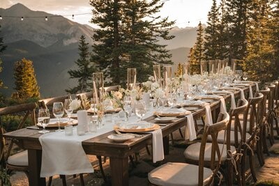 A long outdoor reception table is set with candles, flowers and place settings beside the mountains.