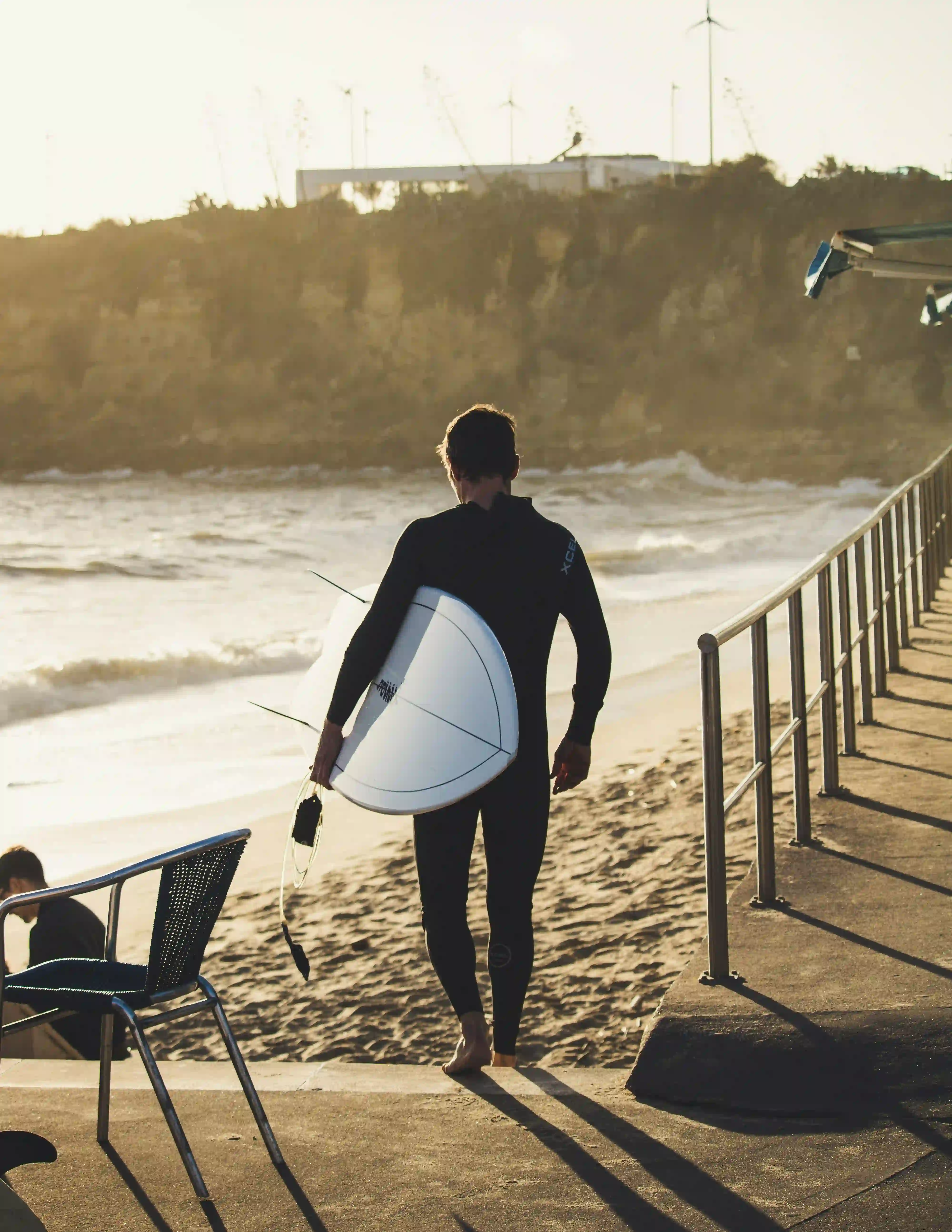 Surfer walking barefoot toward the beach carrying a surfboard at sunset.