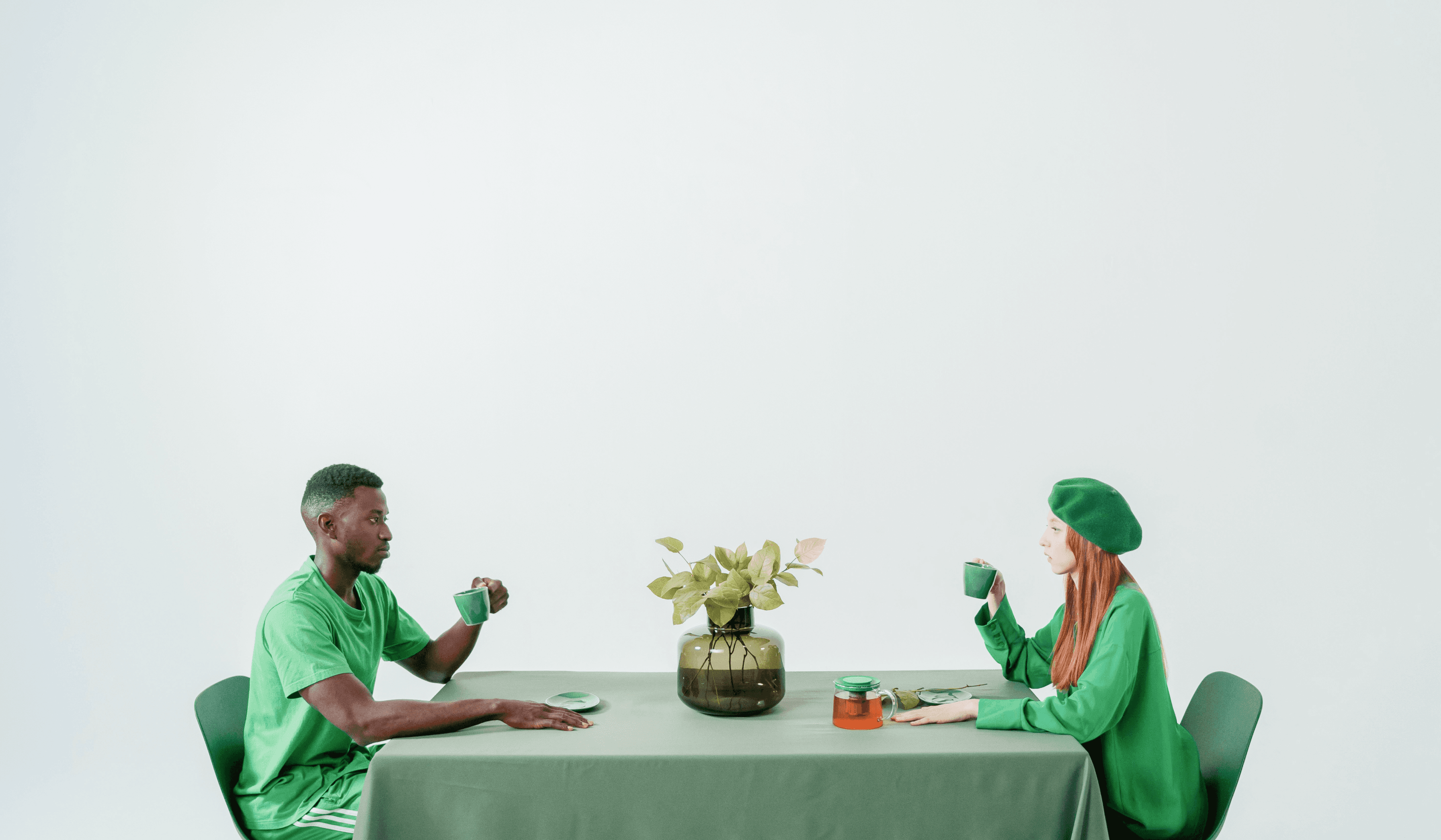 A man and woman in green are having tea at a long dining table