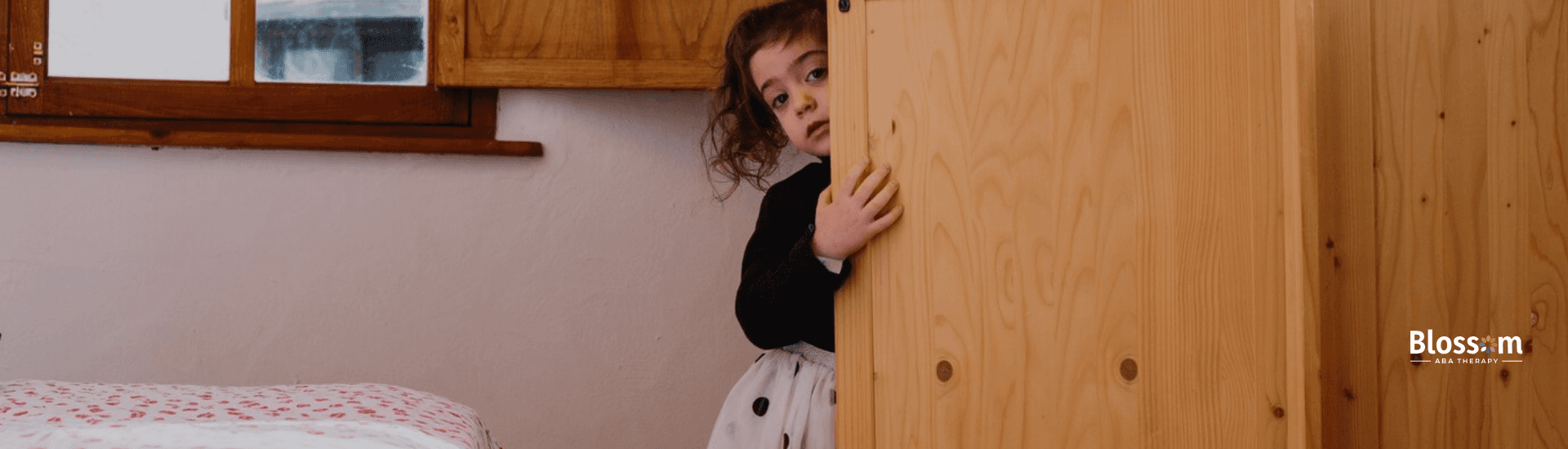 A little girl hising behind a cabinet door