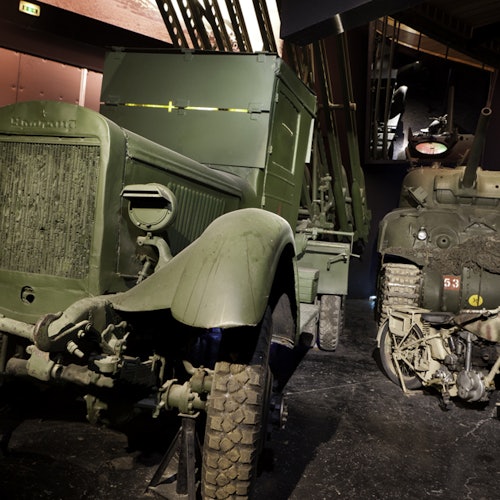 Två vintage militärfordon med grön kamouflagemålning i en svagt upplyst museiutställning. Text på fordonets grill lyder "Studebaker."