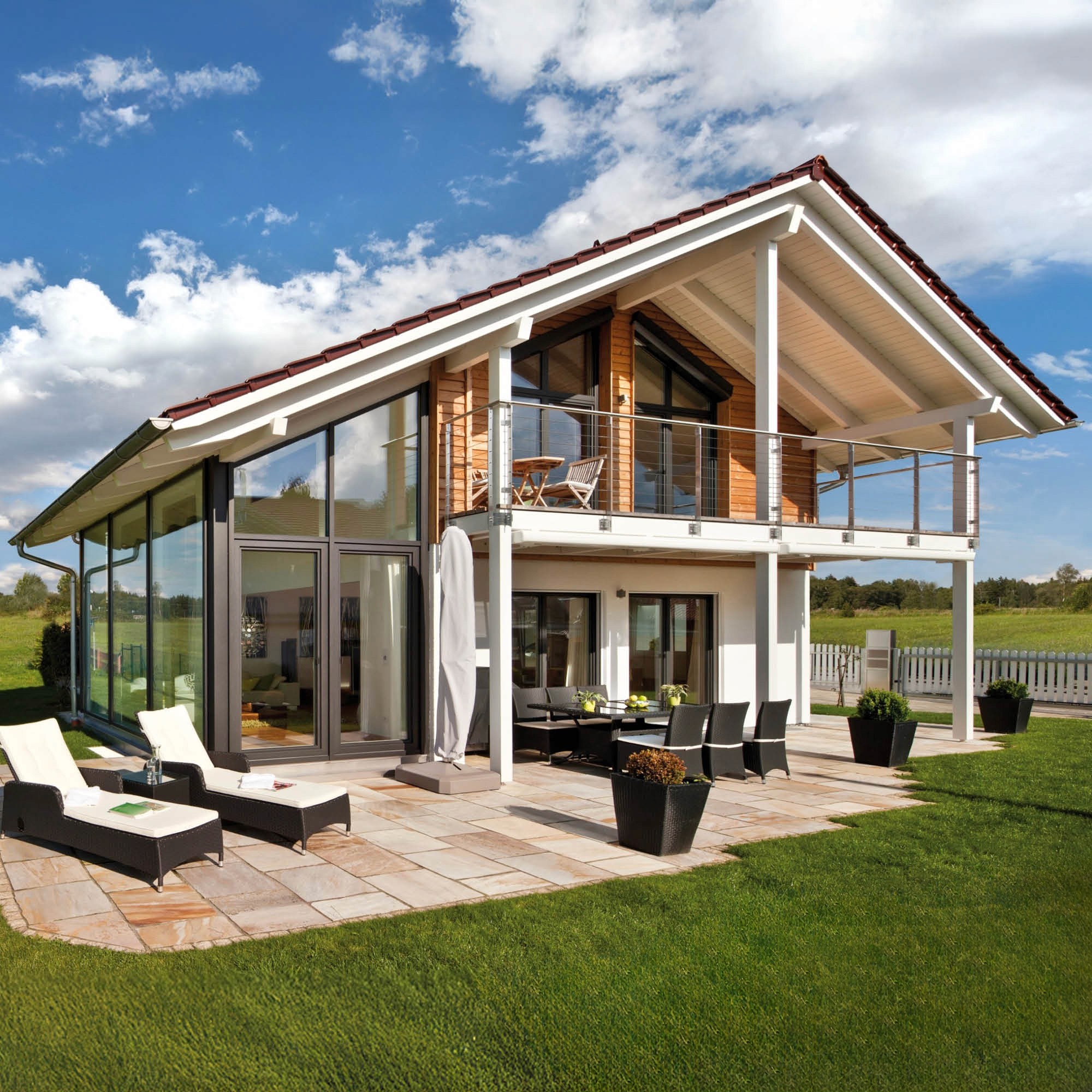 Modernes Holzhaus mit großen Glasflächen, Balkon, Terrasse mit Möbeln und gepflegtem Garten.