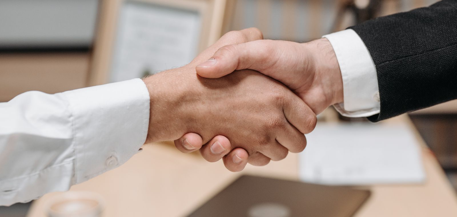 Two business people shaking hands over a desk after closing a deal