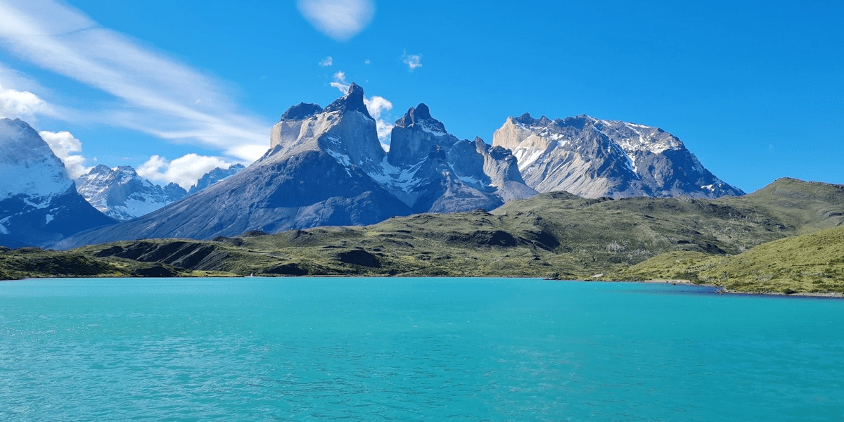 Turquoise lake with rugged snow-capped mountains under bright blue sky, scenic natural landscape.