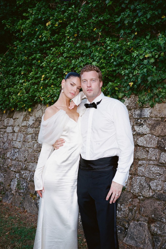Bride and groom posing together against a stone wall during an outdoor wedding portrait