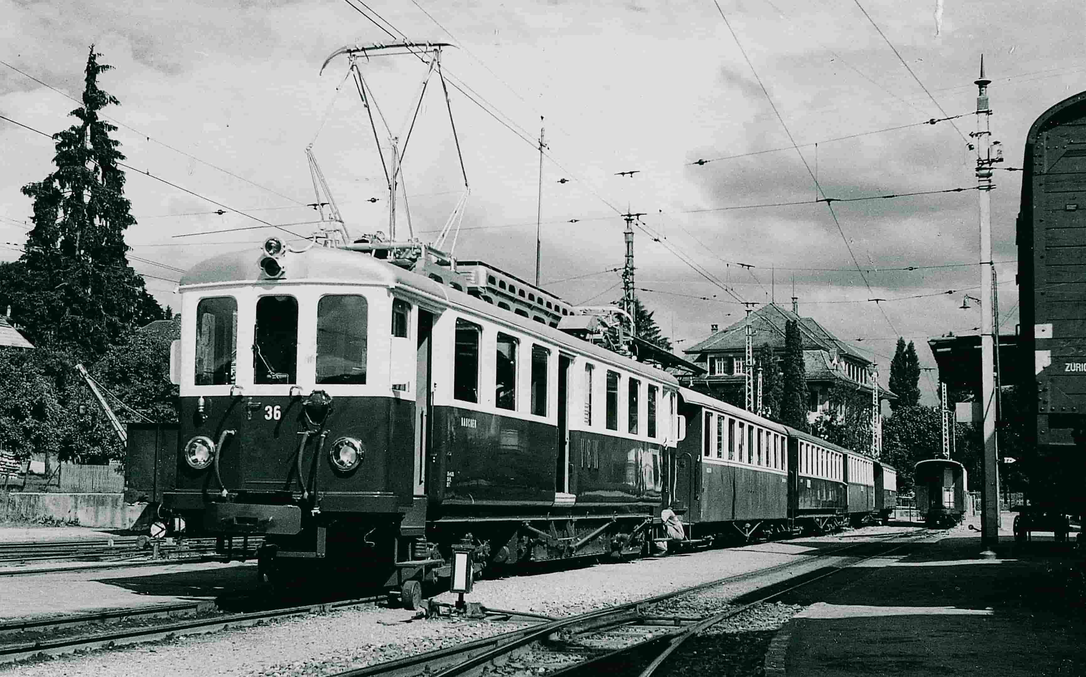 Schwarz Weisses historisches Bild von einem Triebwagen an einem Bahnhof.